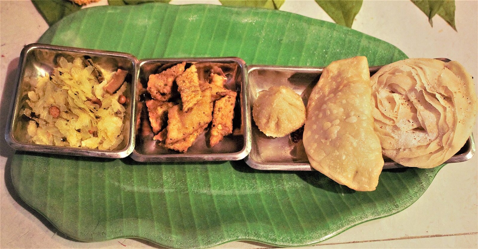A large brass thali laid out with traditional Diwali faral — chakli, karanji, chivda, ladu and shankarpali
