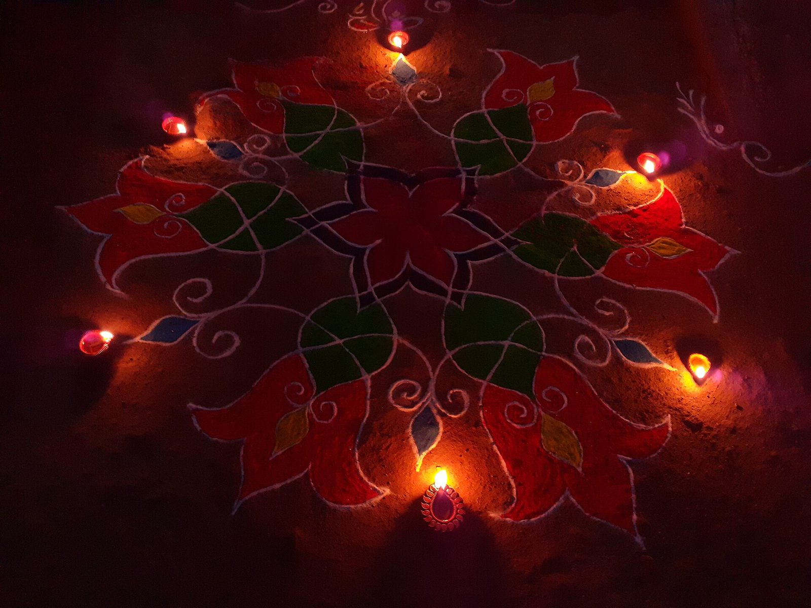 A colourful rangoli surrounded by lit clay diyas